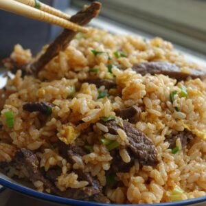 Savoury beef fried rice garnished with scallions and served with chopsticks.