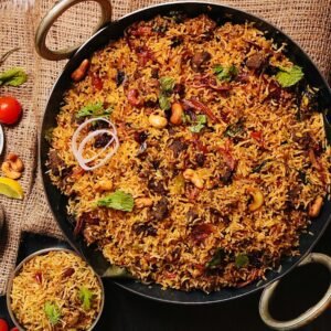 Top view of flavorful Indian biryani in a cooking pan, garnished with cashews and herbs.
